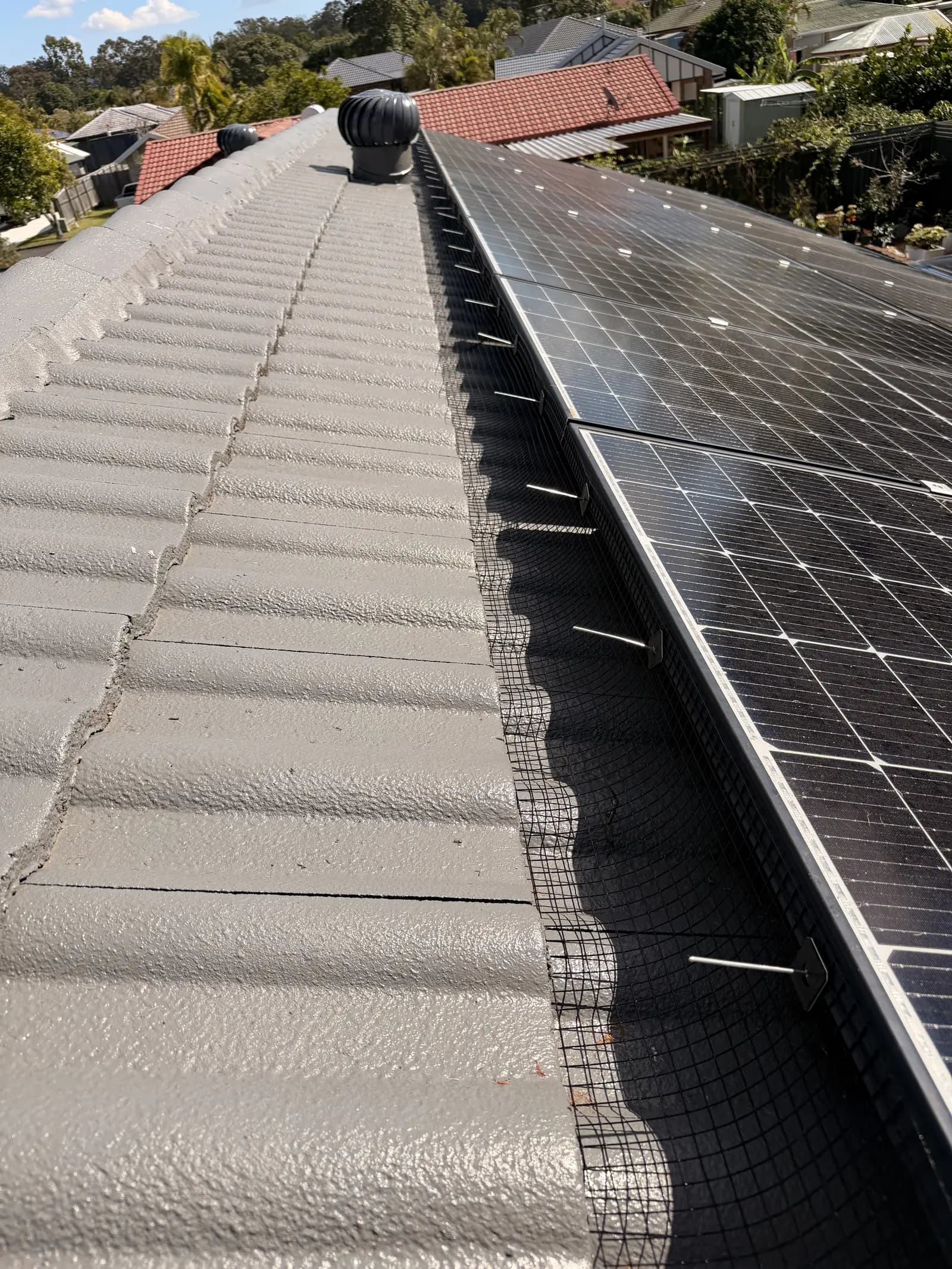 Bird proofing mesh clipped along the lower edge of a rooftop solar array, with the clips visible against the tile roof